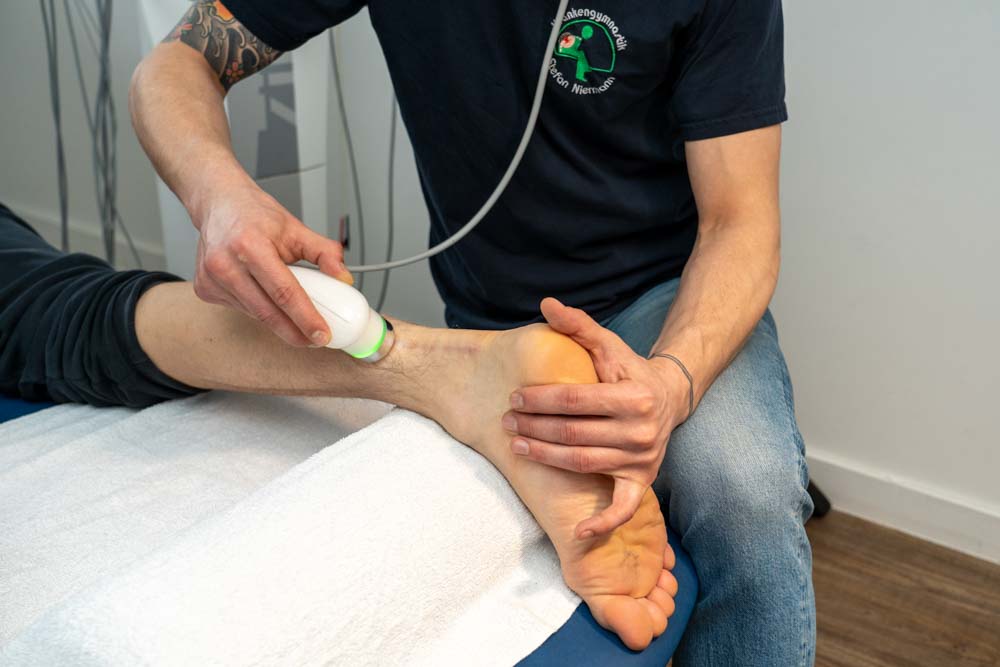 Physiotherapeut verwendet ein Ultraschallgerät, um den Fuß eines Patienten zu behandeln.