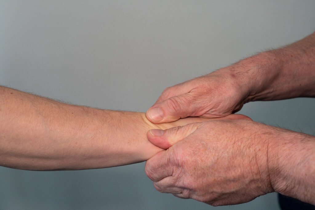 Physiotherapeut übt Druck auf den Unterarm eines Patienten aus.